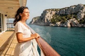 Femme en robe blanche admirant les côtes corses depuis le pont d'un bateau de croisière tout inclus en Méditerranée