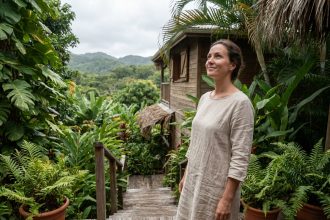 Femme en robe de lin sur la terrasse en bois d'un gîte écoresponsable entouré de végétation tropicale en Guadeloupe