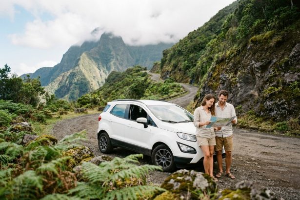 Couple debout à côté d'un SUV blanc sur une route de montagne verdoyante à La Réunion, entouré de végétation tropicale et de roches volcaniques