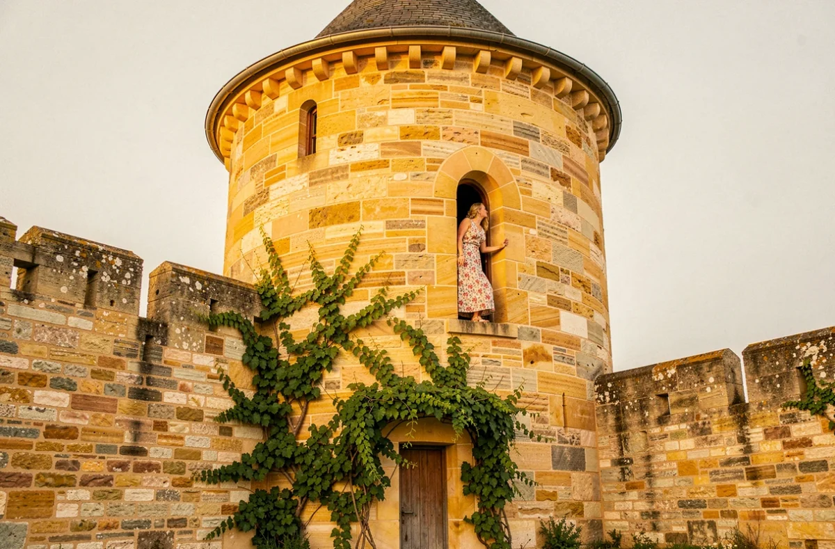 Tour médiévale d'Oingt en pierres dorées du Beaujolais avec femme à la fenêtre cintrée et vigne sur la façade